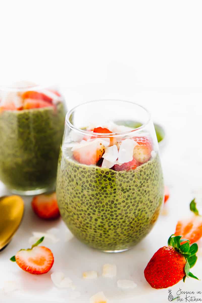 Two glasses of matcha chia pudding, topped with strawberries and coconut flakes. 