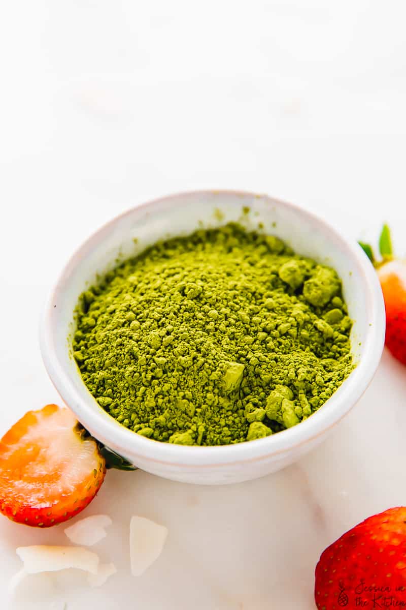 Bright green matcha green tea in a bowl surrounded with strawberries.