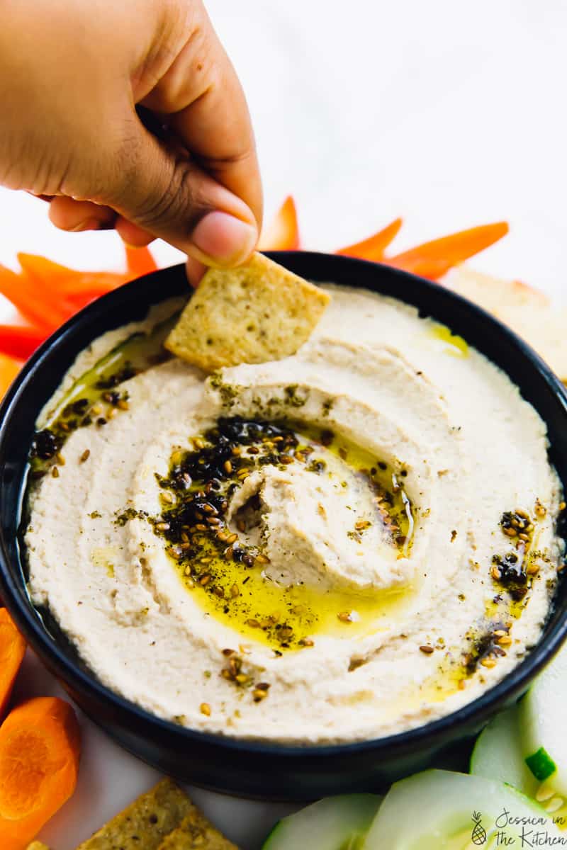 Hand dipping a chip into a bowl hummus.
