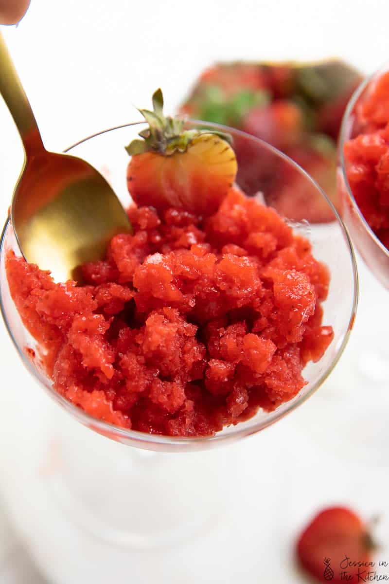 A spoon scooping out some strawberry granita form a glass. 