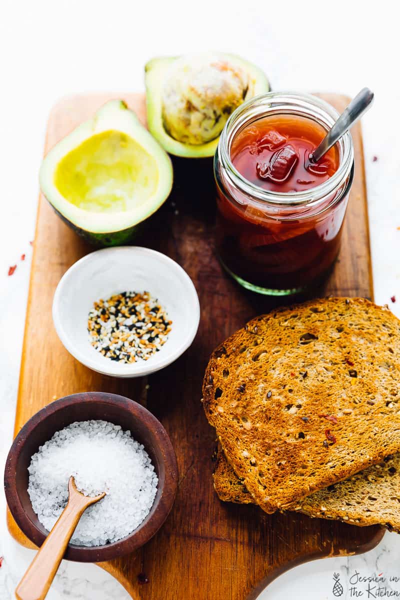 ingredients for an avocado toast: bread, pickled onions, avocado halves, everything bagel seasoning and sea salt