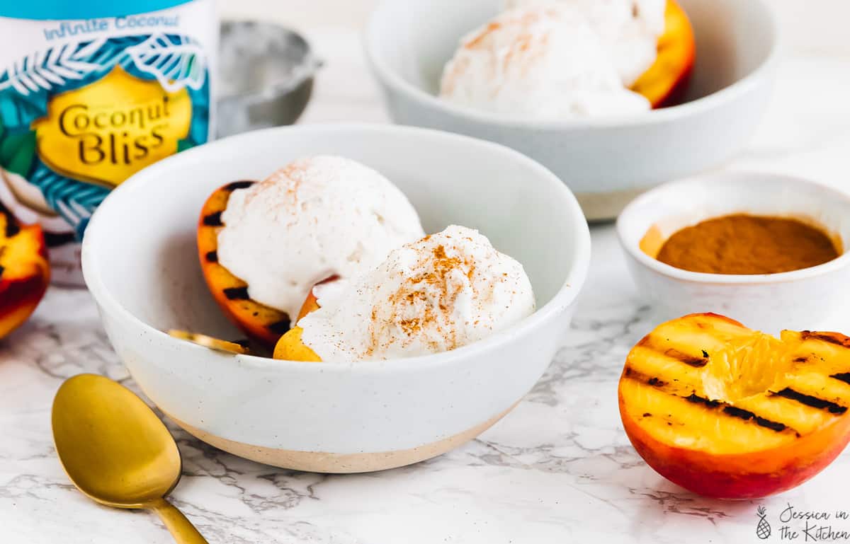 A bowl of grilled peaches topped with ice cream. 