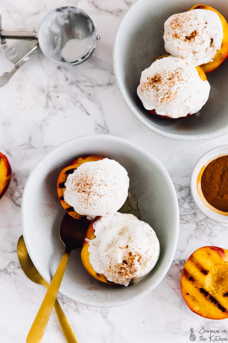 Top down view of grilled peaches in bowls, topped with ice cream.
