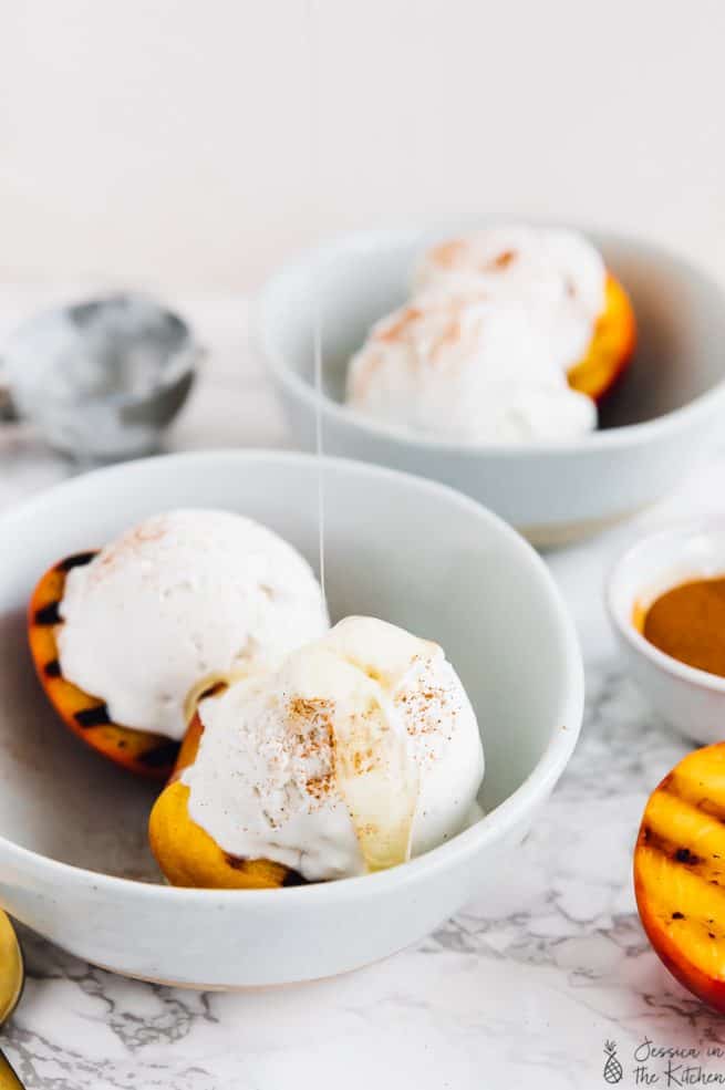 Grilled peaches and coconut ice cream in a bowl with maple syrup drizzled on top.