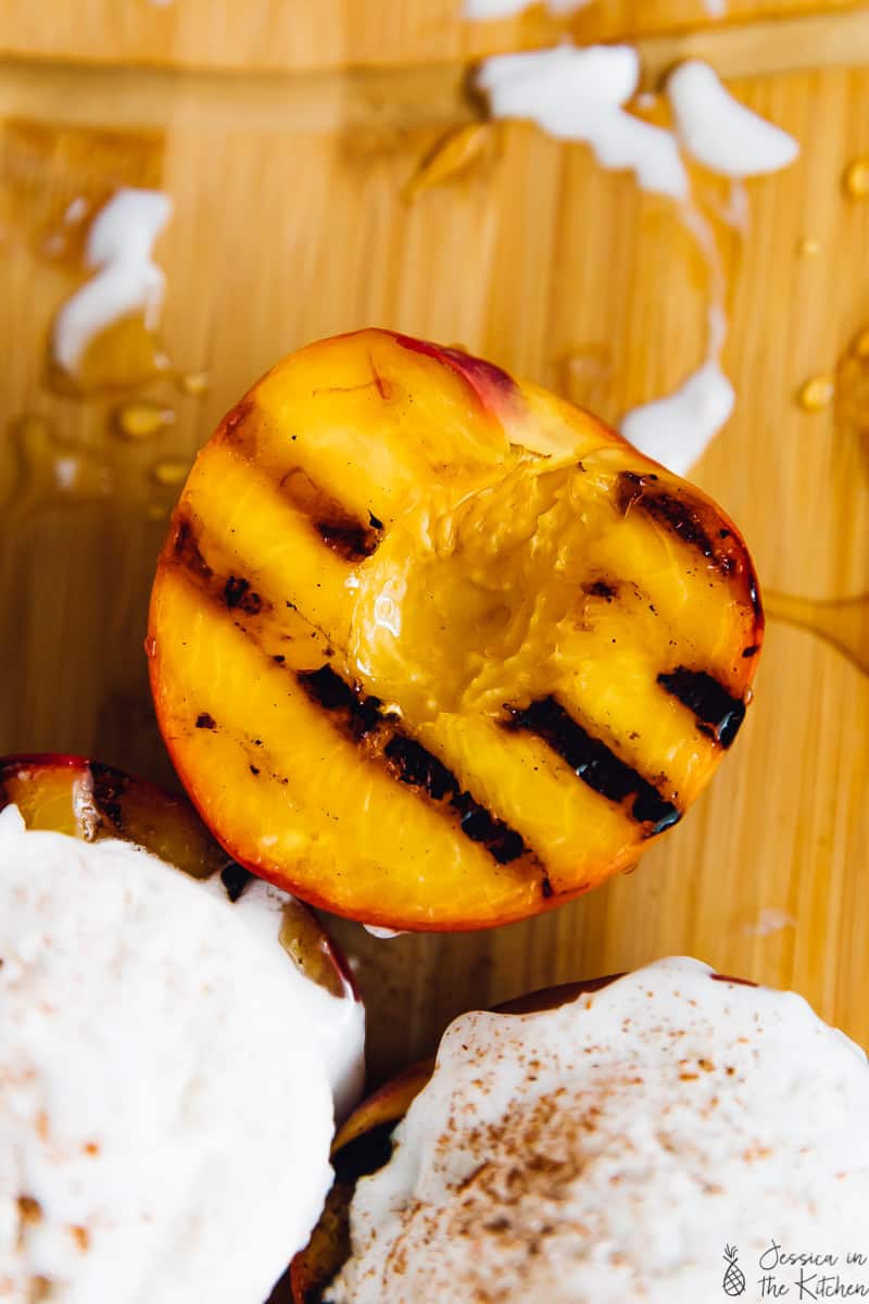 Overhead shot of grilled peaches, some topped with ice cream. 
