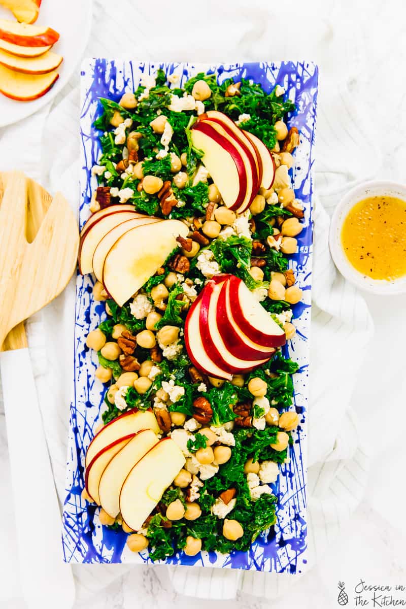 Overhead view of kale apple salad topped with chickpeas and vegan feta on a rectangular platter.