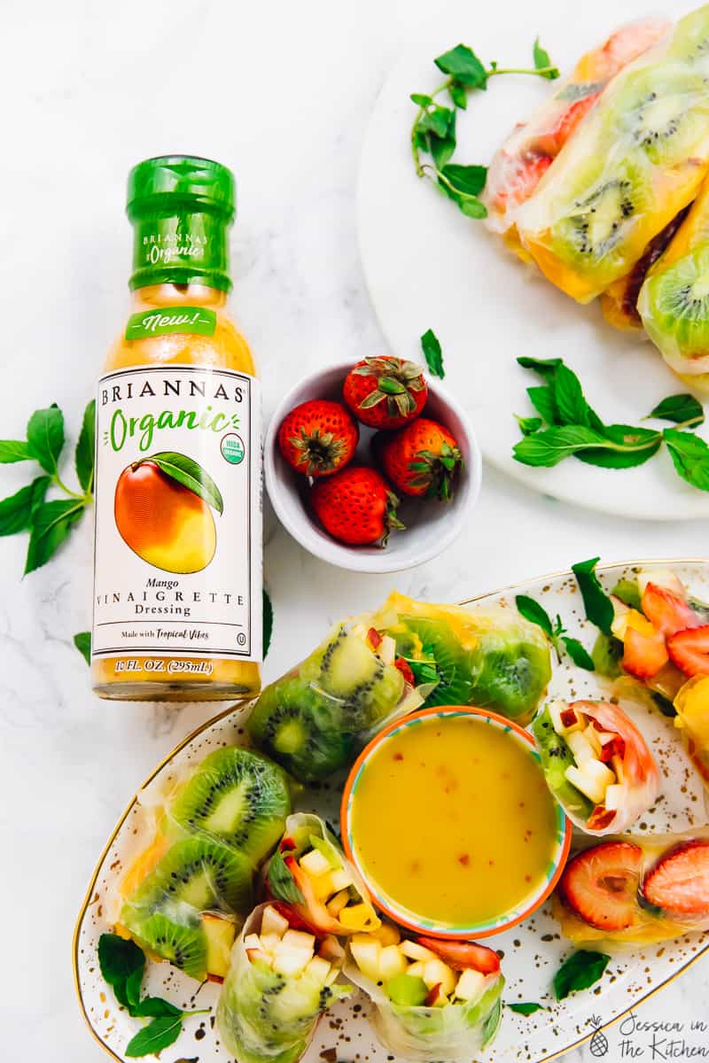 Top down shot of fruit spring rolls on platters, next to a bottle of dressing. 