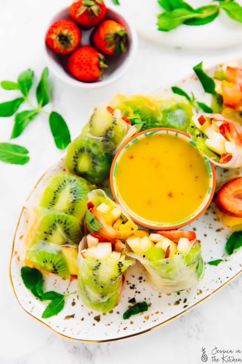 Plate of assorted fruits wrapped in spring roll wrappers with a mango dressing , some cut in half. summer fruit spring rolls.