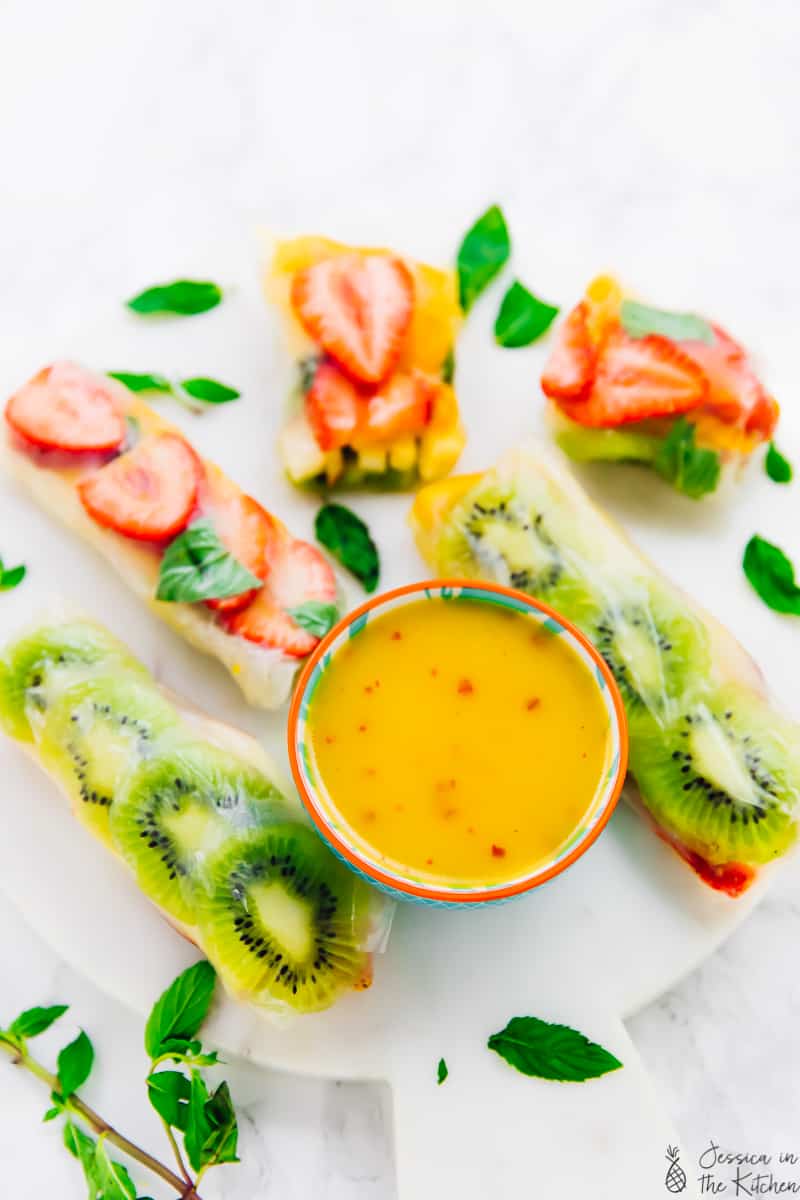 A plate of assorted fruits wrapped in spring roll wrappers with a mango dressing , some cut in half.