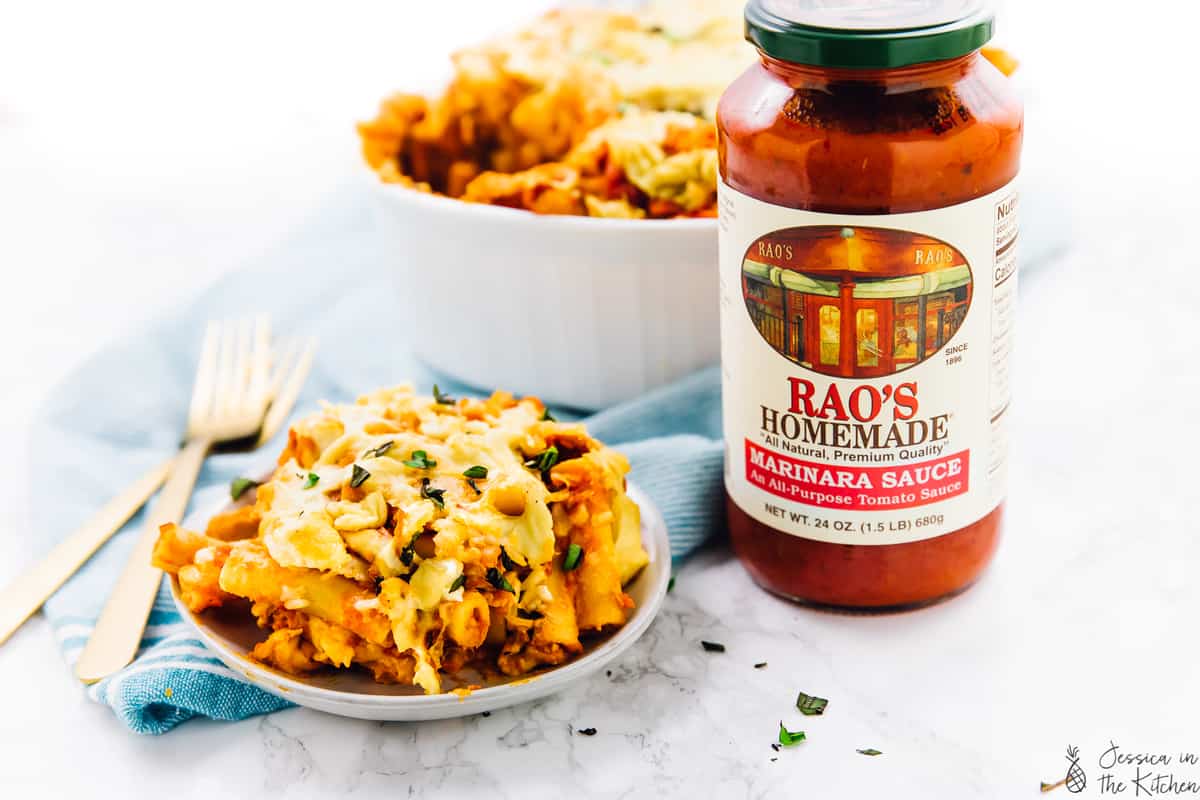 Cheesy baked ziti with rao's homemade marinara sauce jar beside it.