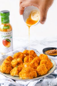mango sauce being drizzled onto a plate of cauliflower wings