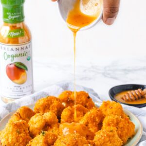 mango sauce being drizzled onto a plate of cauliflower wings