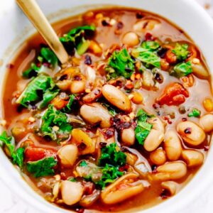 A bowl of white bean and kale soup with a spoon in it.