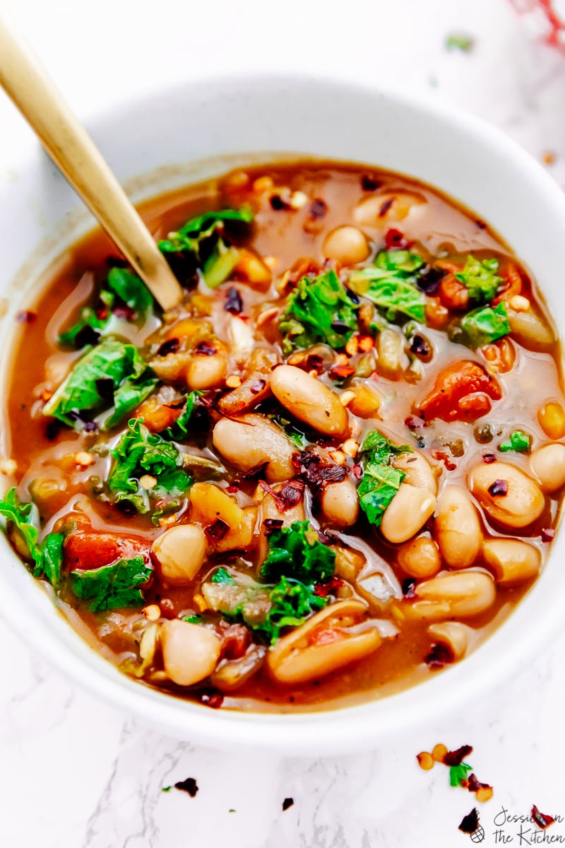 A spoon in a bowl of white bean and kale soup. 