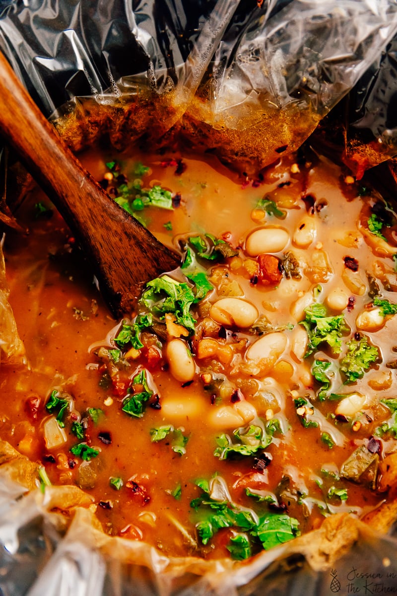 A wooden spoon stirring soup in a slow cooker.