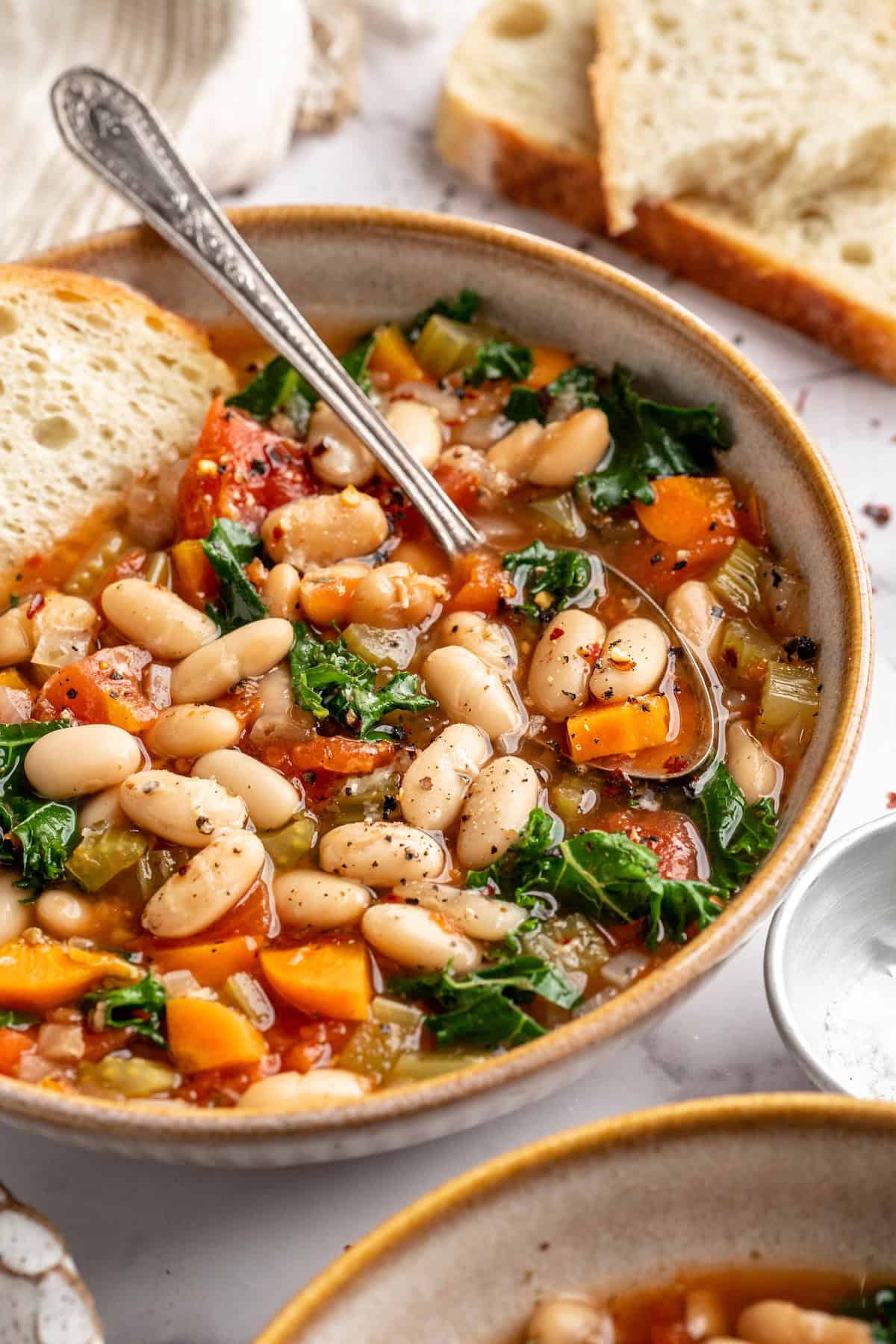 White bean and kale soup in bowl with spoon and slice of bread
