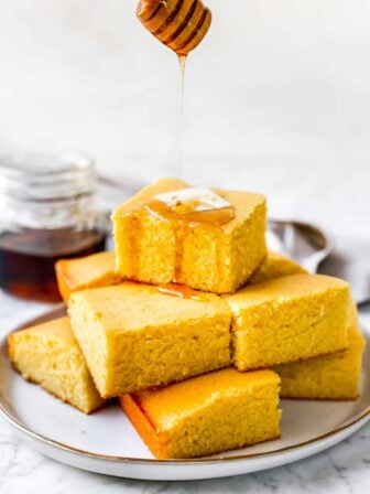 Cornbread muffins in a stack with maple syrup drizzled on top and a pat of butter.