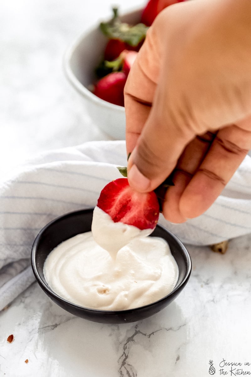 A hand dipping a strawberry into cashew whipped cream.