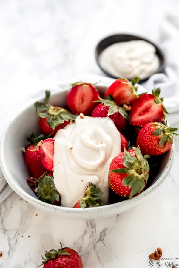 A bowl of strawberries, topped with cashew whipped cream.