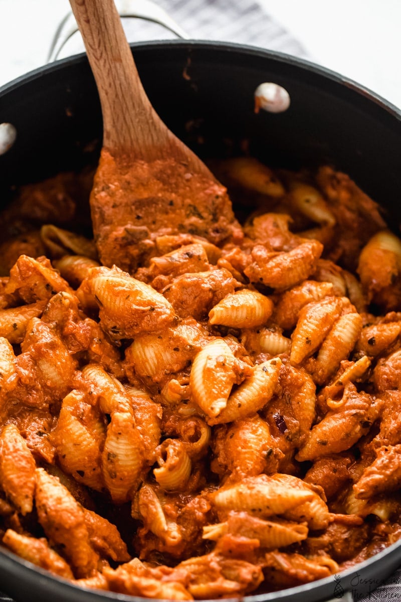 Wood spoon stirring a pot of cooked creamy tomato pasta.