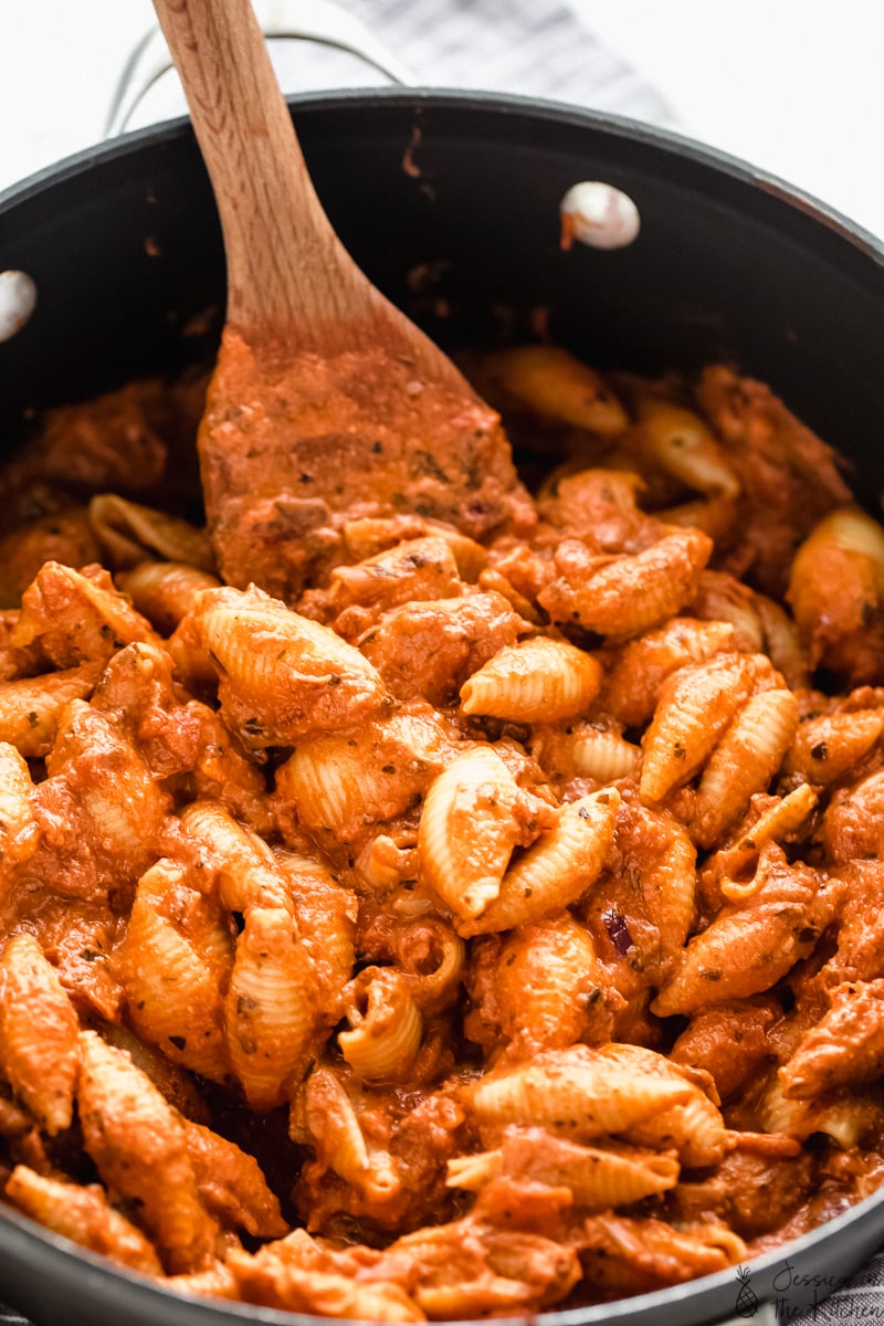 Pot of cooked creamy tomato pasta being stirred by a wooden spoon. 