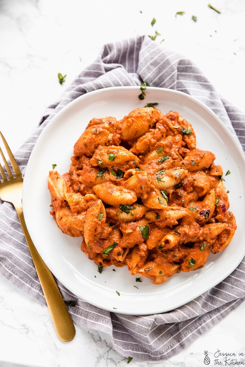 Top down view of creamy tomato pasta on a white plate with a gold fork on the side. 