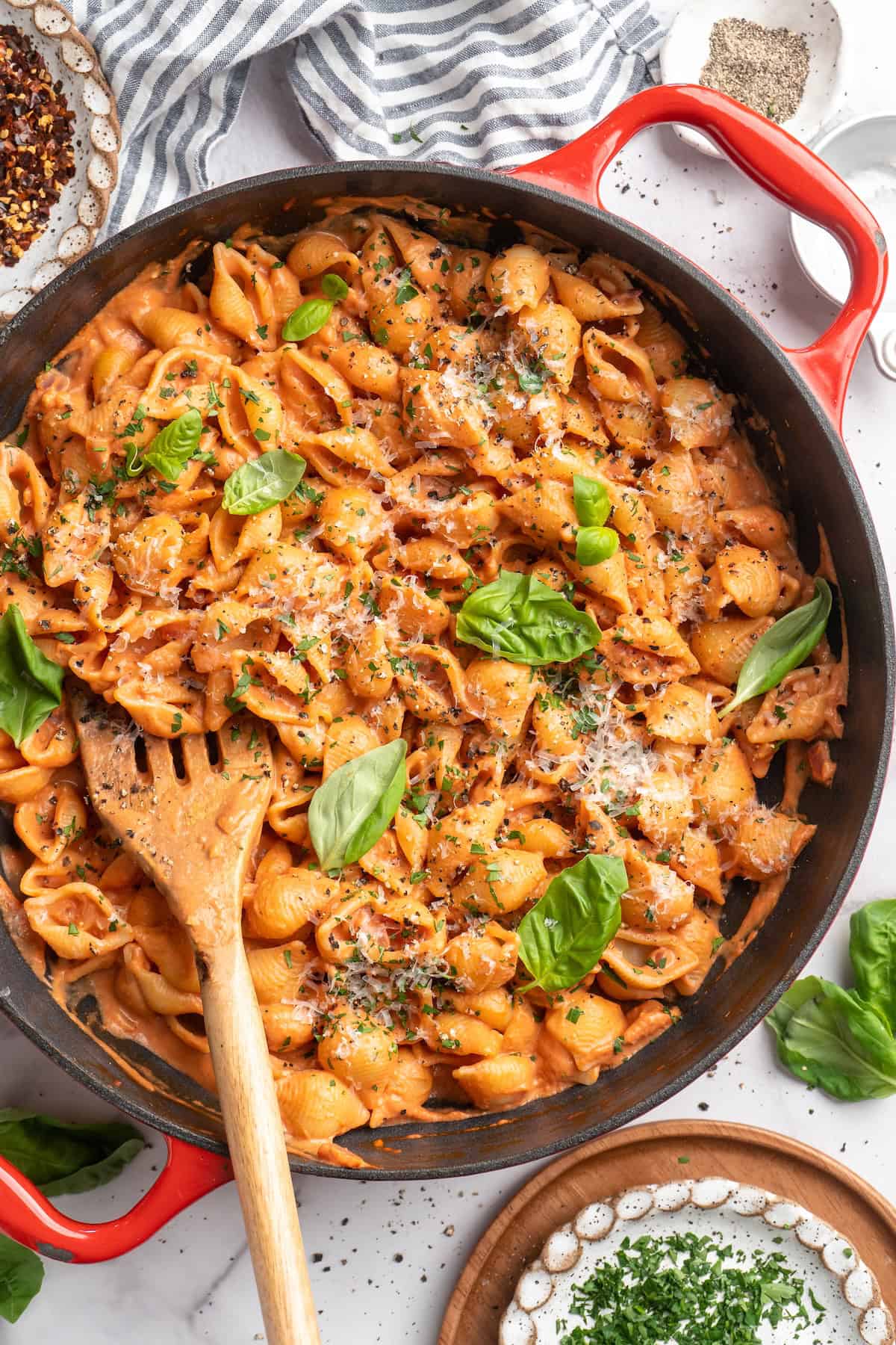 Overhead view of creamy tomato pasta in skillet with fresh basil leaves and vegan Parmesan