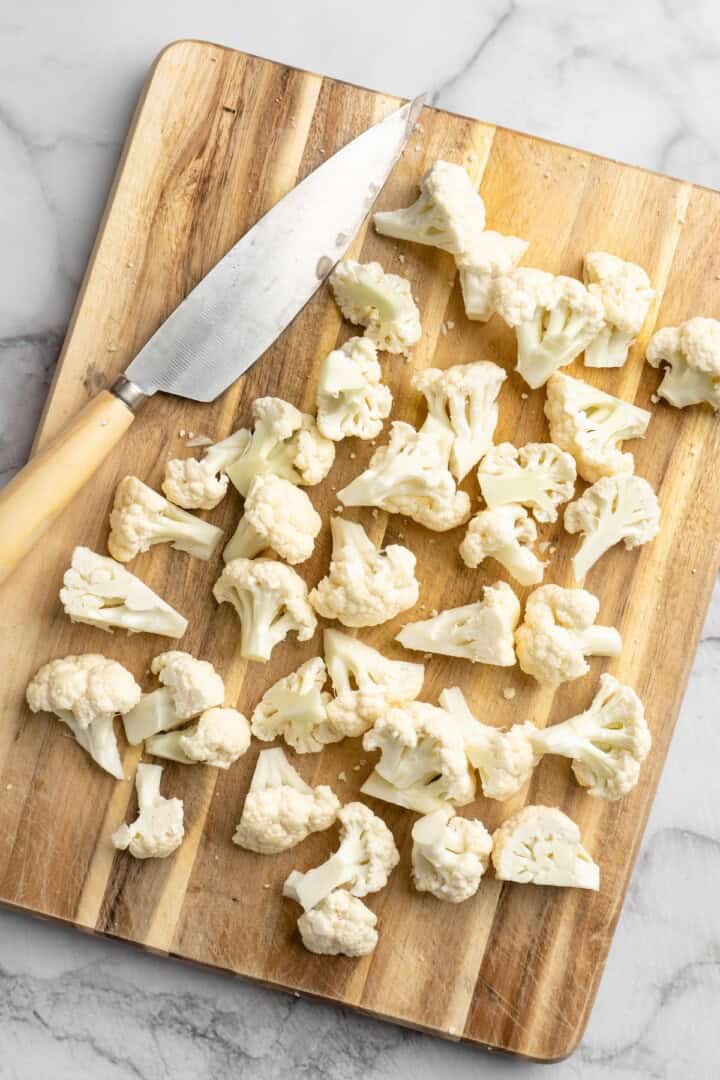 Overhead view of cauliflower florets on cutting board with knife