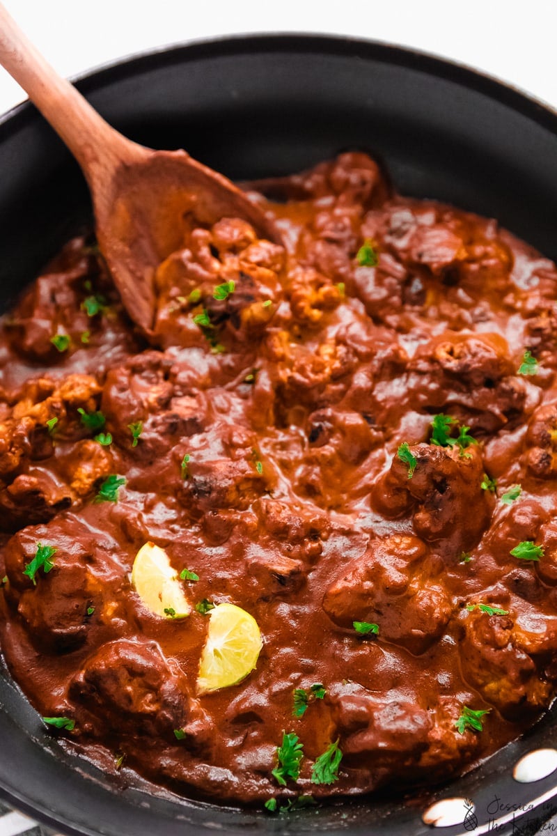 cauliflower in an indian butter sauce in a pan with limes and chopped parsley