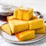 cornbread muffins in a stack with maple syrup drizzled on top and a pat of butter