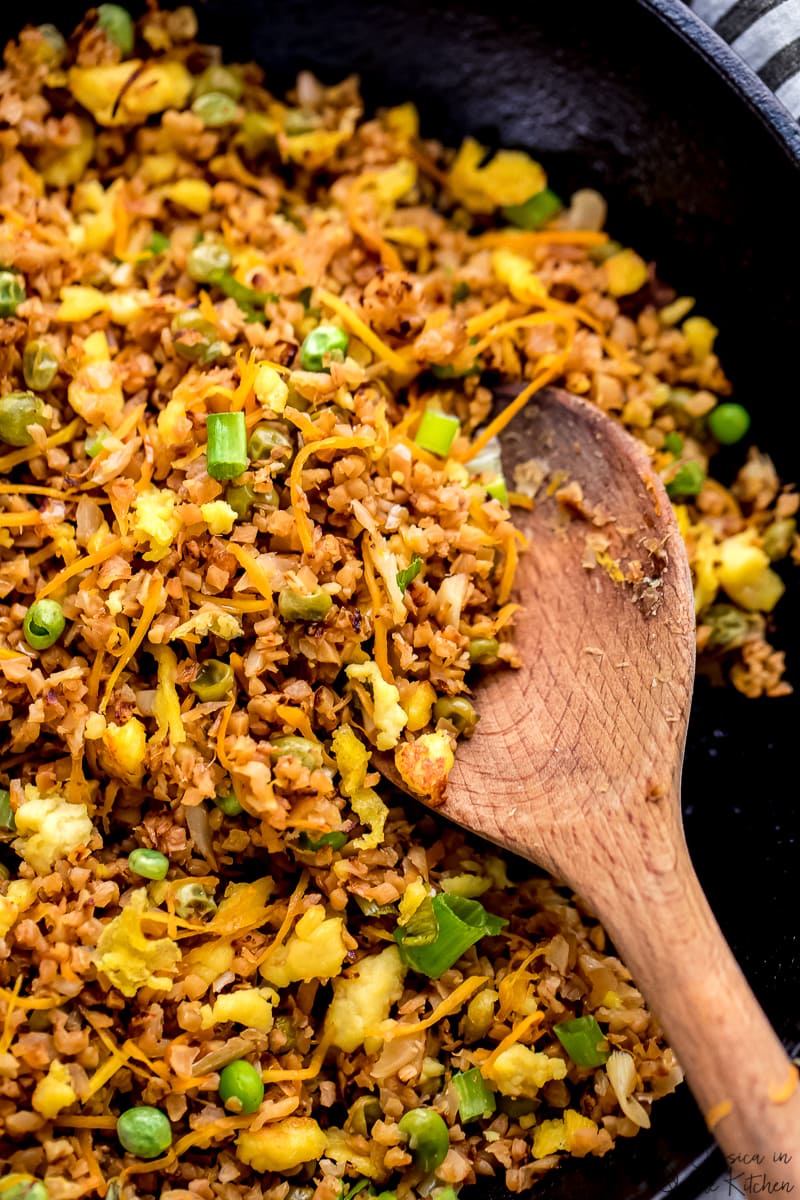 A spoon stirring some vegan fried rice in a black skillet. 