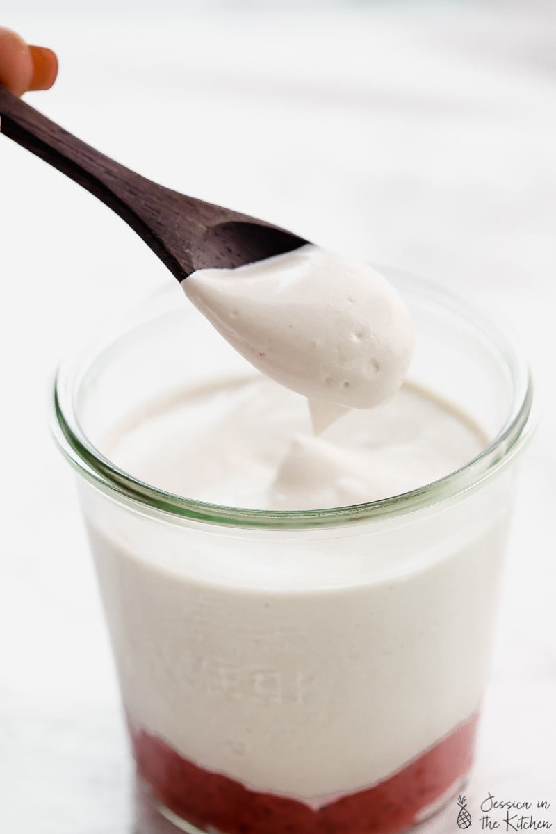 A spoon scooping out some vegan yogurt from a glass. 