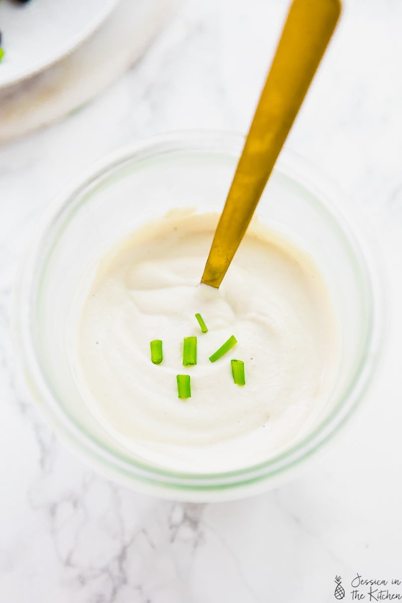 Overhead view of vegan sour cream in a glass pot with a gold spoon in it. 