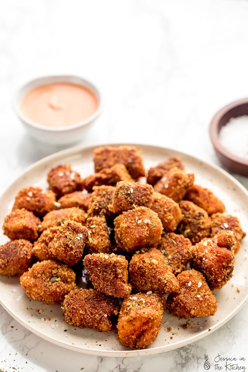 Vegan chicken nuggets on a plate with a dip in the background a plate of sprinkling salt.