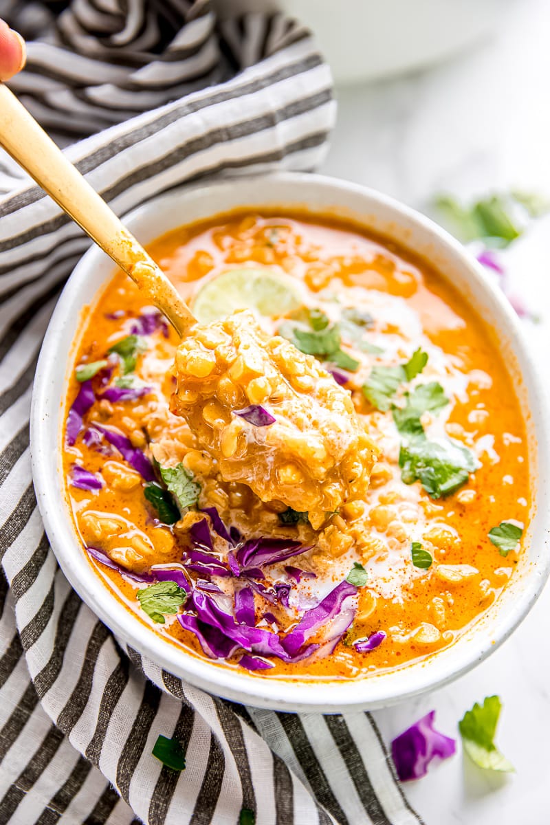 A bowl of coconut curry lentil soup, topped with cabbage, parsley, and coconut milk, with a spoon taking a spoonful out