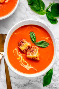 A bowl of creamy tomato soup topped with cheesy croutons.