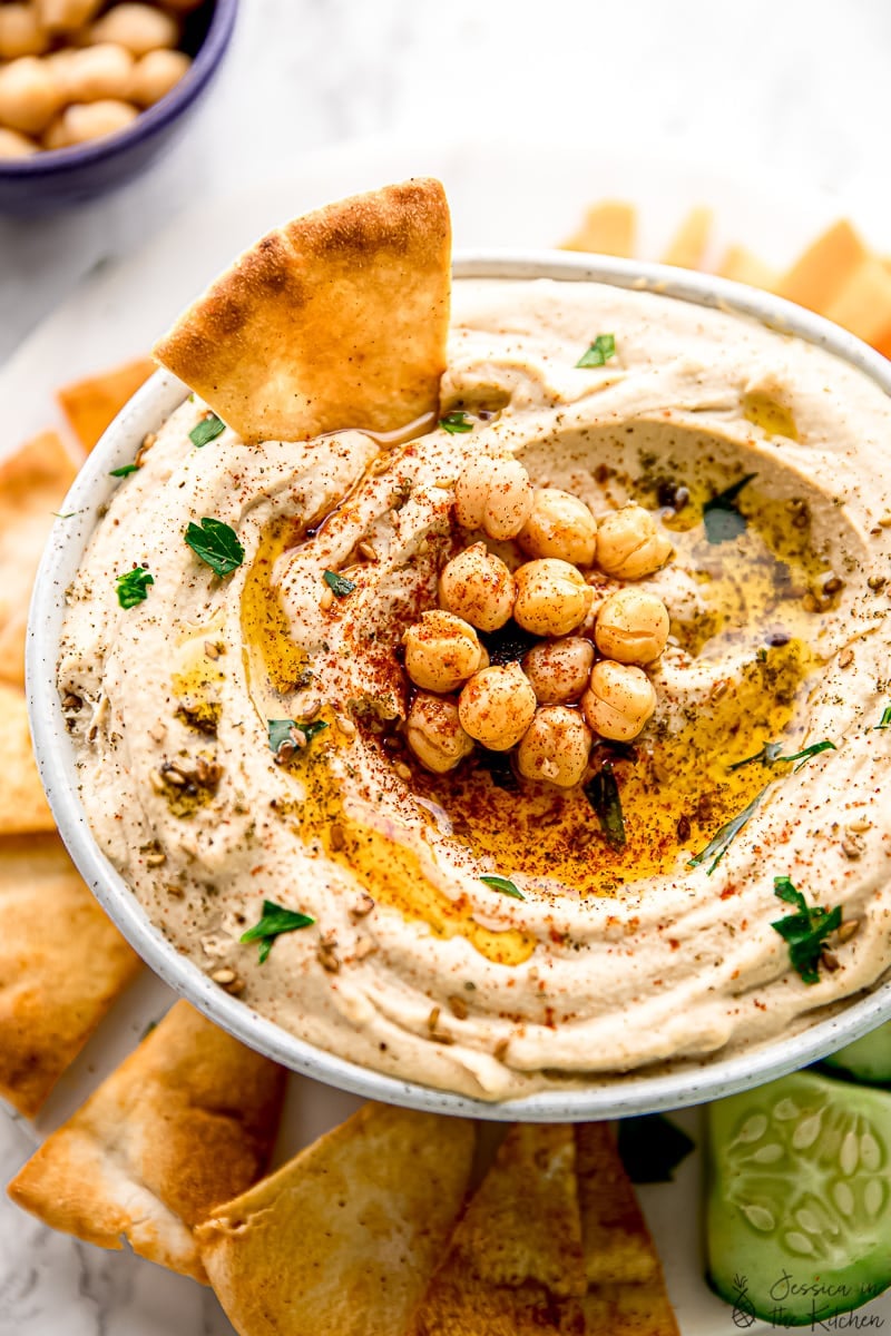 A bowl of hummus, topped with chickpeas and surrounded by pita chips. 