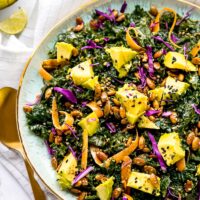 Overhead view of kale salad topped with avocado, carrots, seeds, and dressing in a large serving bowl.