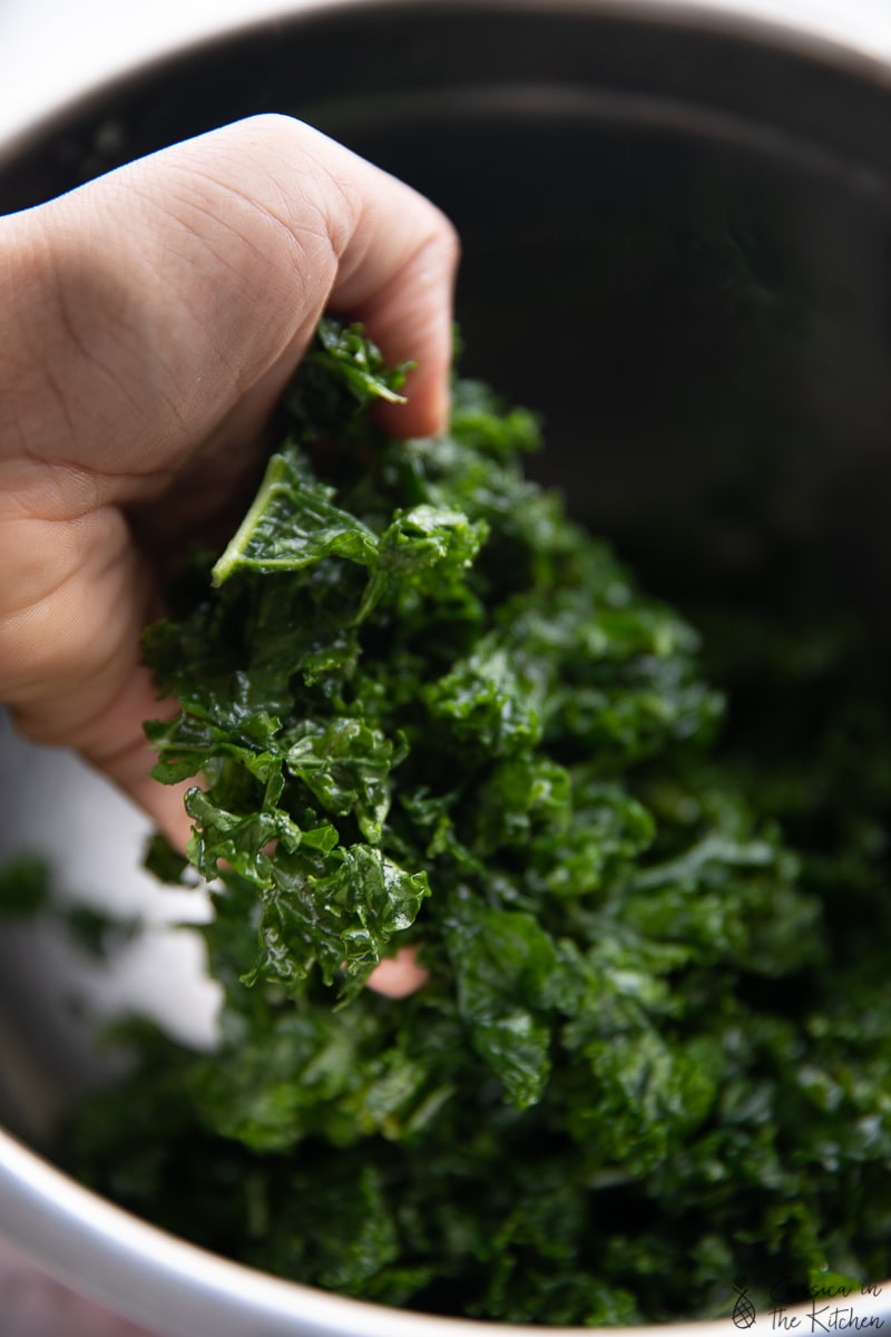 A hand massaging kale leaves in a metal bowl.