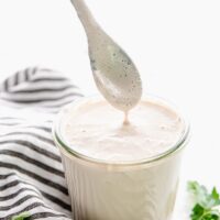 A spoon drizzling alfredo sauce into a glass.