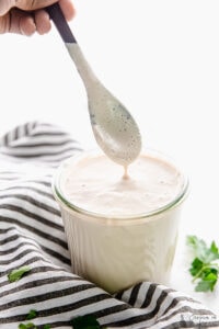 A spoon drizzling alfredo sauce into a glass.
