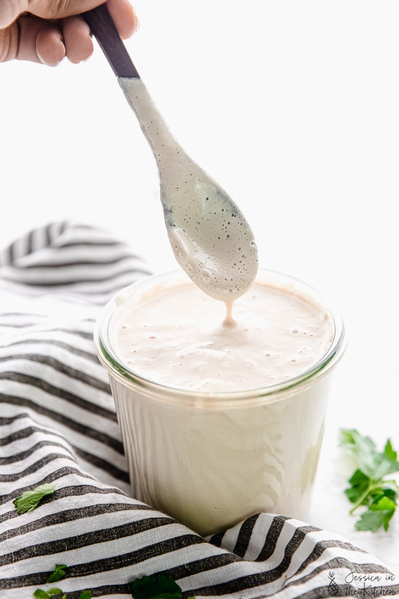 A spoon drizzling vegan alfredo sauce into a glass. 