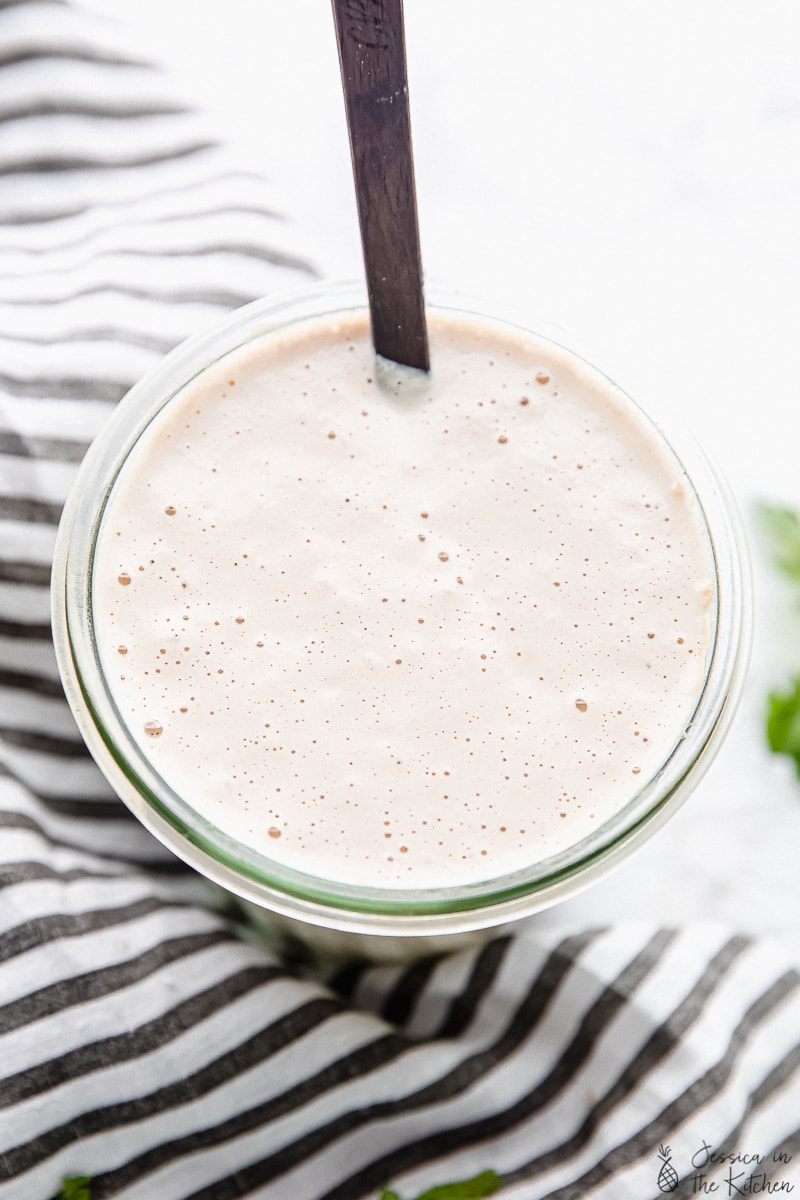 Top down shot of vegan alfredo sauce in a glass with a spoon.