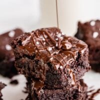 Vegan brownies stacked on each other as chocolate drizzles over it.