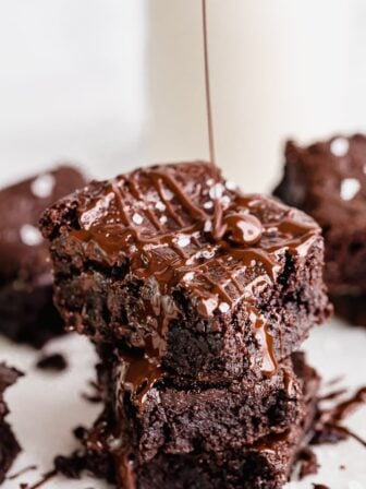 Vegan brownies stacked on each other as chocolate drizzles over it.