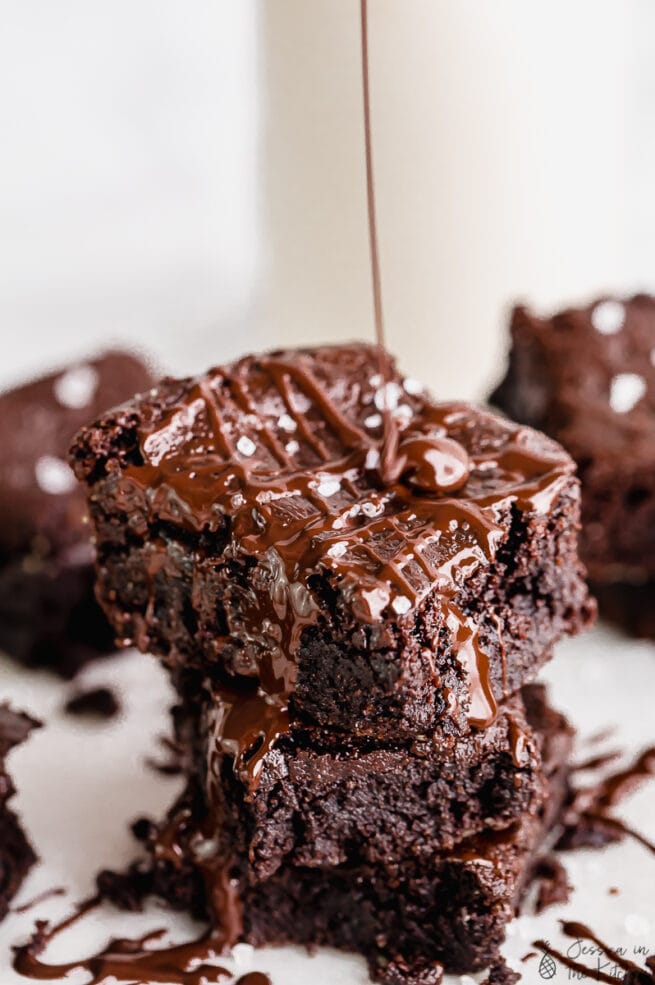 Vegan brownies stacked on each other as chocolate drizzles over it.