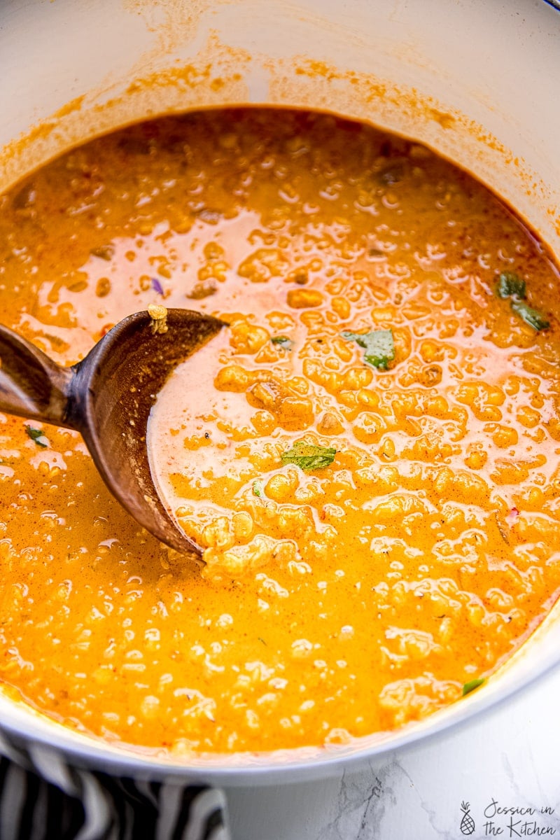 A serving spoon stirring coconut curry lentil soup in a big bowl. 