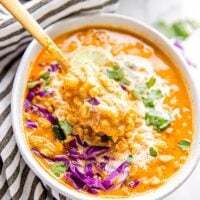 Vegan curry soup in a bowl with a spoon pulling some out.