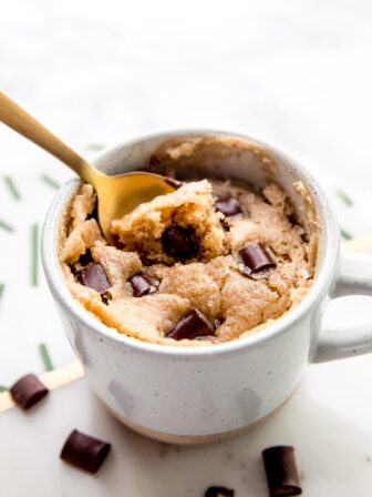 A gold spoon scooping into a vegan chocolate chip mug cake.
