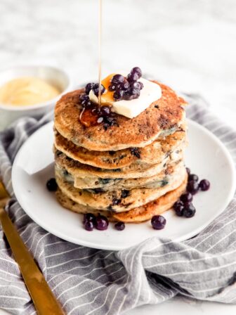 A stack of vegan blueberry pancakes with syrup and blueberries.